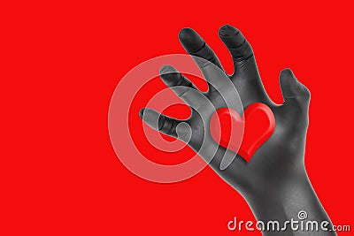 Heart in a black gloved hand isolated on red Stock Photo