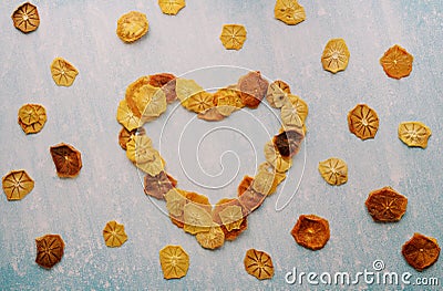 Heart of fruit chips framed with pieces of dried fruit on a blue scratched background Stock Photo