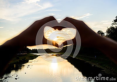 Heart gesture in front of sunset above river. Idea honeymoon travel. Honeymoon summer resort. Romantic date ideas. Hands Stock Photo