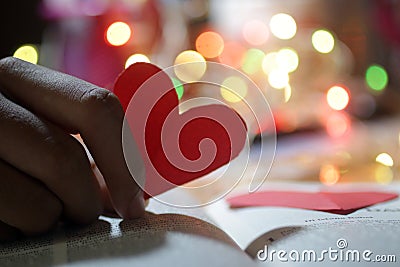 Heart in hand. Red love shaped paper on bright colorful bokeh background. Blank paper with hope and love symbol in hands. Copy Stock Photo
