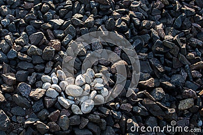 Heart is laid out of white rounded stones against dark brown and gray granite of railway embankment Stock Photo