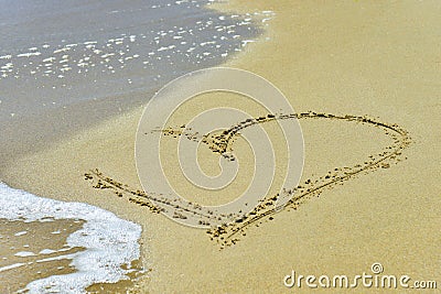 A heart on the sand is washed away by the waves on the shore Stock Photo