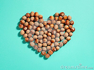 Heart shape made of unpeeled hazelnuts casts shadows on a turquoise paper background. Nuts as an antioxidant and protein source Stock Photo