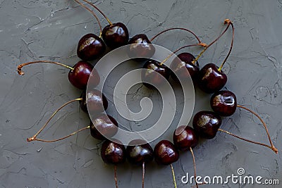 Heart shaped cherries with stalks close up as concept of berries loving. Grey old stone dark backdrop Stock Photo