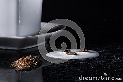 A heart shaped coffee cup with coffee beans, spilled milk and brown sugar on a black background with silver lining. Stock Photo