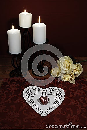 Heart shaped dollie and gemstone, three white candles in metal holders and bouquet of yellow roses on wooden table. Stock Photo