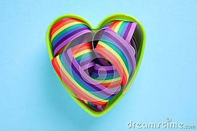 Heart shaped mold with bright rainbow ribbon on color background. Symbol of gay community Stock Photo