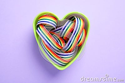 Heart shaped mold with bright rainbow ribbon on color background. Symbol of gay community Stock Photo