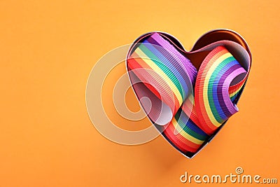 Heart shaped mold and bright rainbow ribbon on color background, top view. Symbol of gay community Stock Photo