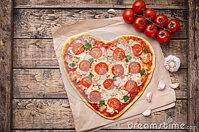 Heart shaped pizza margherita love food symbol with mozzarella, tomatoes, parsley, and garlic composition on cutting Stock Photo