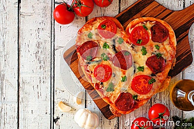 Heart shaped pizza for Valentines Day over white wood, above view, side border table scene Stock Photo