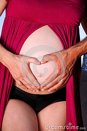 Heart shaped pregnancy. Hands of future parents is making heart symbol on pregnant tummy. Stock Photo