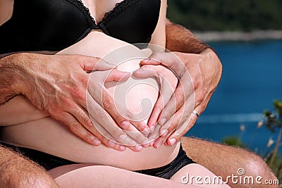 Heart shaped pregnancy. Hands of future parents is making heart symbol on pregnant tummy. Stock Photo