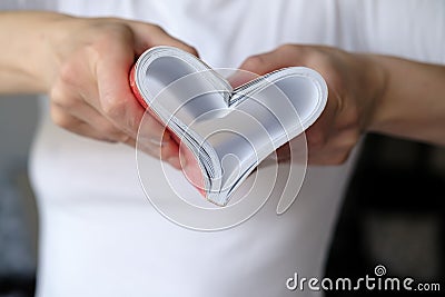 Heart is a symbol of love made of bent sheets of a notebook, female hands are holding near the chest. Valentine`s Day. Stock Photo