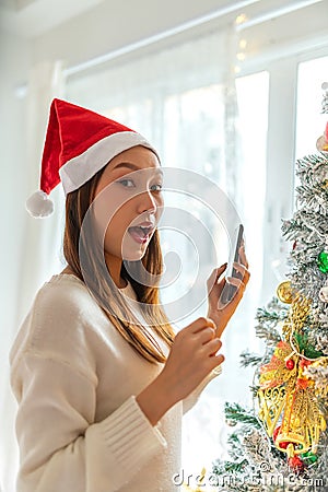 Christmas Magic. Asian Woman in Santa Hat Captures Festive Tree Moments on Phone Stock Photo