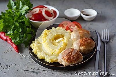 A hearty lunch: mashed potatoes, pork cutlets, tomato slices in a plate, tomato salad in a white bowl, fresh greens on a Stock Photo