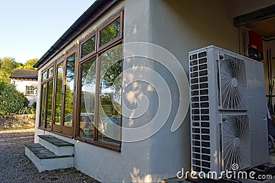 Heat pump warming a house on a cold Autumn day. External view of the fan unit next to the home's windows. Stock Photo