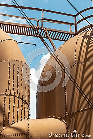 Heavily riveted metal tanks and catwalk, industrial shapes against a blue sky with clouds Stock Photo