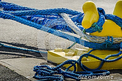 Heavy blue ropes wrap around a yellow mooring bollard on a pier Stock Photo