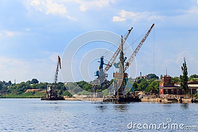 Heavy cranes in cargo port on riverbank Stock Photo