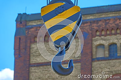 Heavy duty iron hook in a black and yellow fixation in front of an intentionally blurred facade of an industrial building Stock Photo