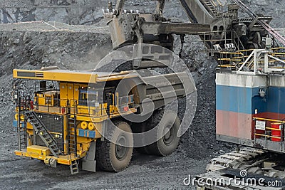 A heavy electric excavator loads ore into a dump truck. Stock Photo