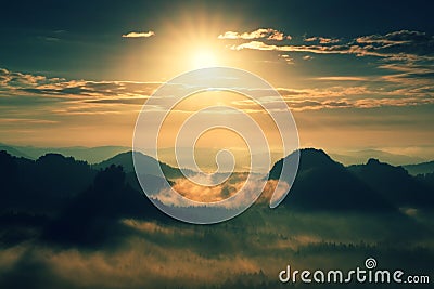 Heavy misty daybreak. Misty sunrise in beautiful hilly park. Peaks of hills are sticking out from dense orange fog. Stock Photo
