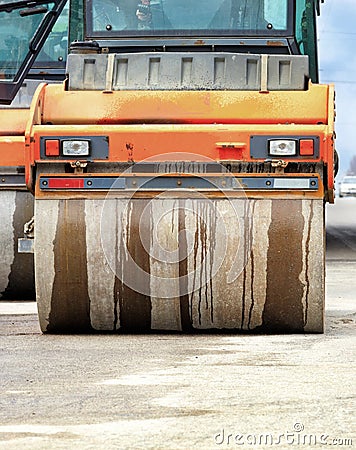 A large and heavy orange vibratory roller is moving along the road Stock Photo