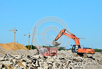 Heavy tracked excavator load stone, old asphalt or concrete waste into a mobile jaw crusher machine. Stock Photo