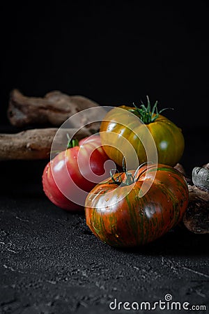 Heirloom tomatoes. Three tomatoes of different colors and a beautiful snag on a black background Stock Photo