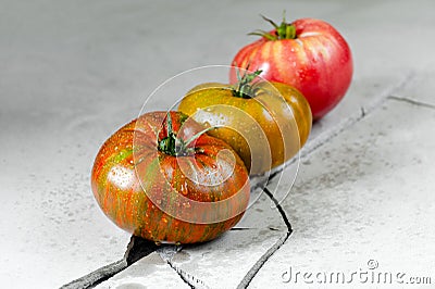 Heirloom tomatoes. Three tomatoes of different colors on a gray concrete table with a crack Stock Photo