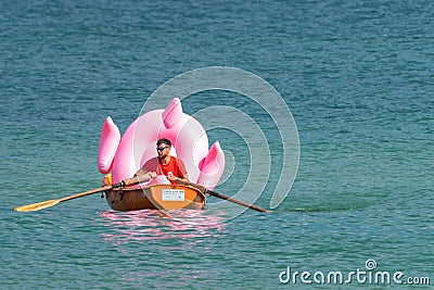 Hel, Poland - 08.01.2021: Beach lifeguard rowing in his orange boat carrying a big pink inflatable flamingo back to the Editorial Stock Photo