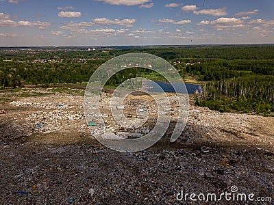 Helicopter aerial view of a big dump with a lot of garbage that pollutes nature, forest and small blue lake under the sky Stock Photo