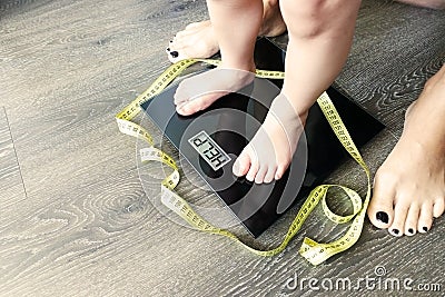 Help fat or obese child with toddler on weight scale, supervised by a parent Stock Photo