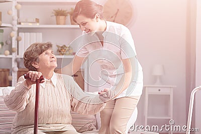 Helpful caregiver supporting smiling senior woman with walking stick Stock Photo