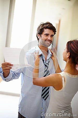 Helping her man dress. Handsome man reading while his wife dresses him. Stock Photo