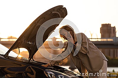 Helpless woman driver calling for help/assistance looking at broken down car, stopped at the roadside Stock Photo