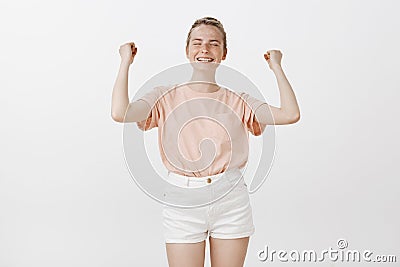 Her dream came true. Good-looking dreamy caucasian female with freckles, smiling joyfully with relief, raising fists in Stock Photo