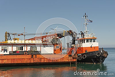 Greek tugboat coming alongside a crane barge to to move the vessel out of port. Editorial Stock Photo