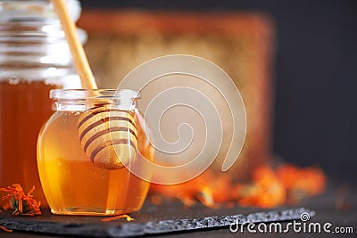Herbal honey in jar with dipper, honeycomb, bee pollen granules, calendula flowers on black background Stock Photo
