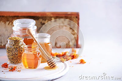 Herbal honey in jar with dipper, honeycomb, bee pollen granules, calendula flowers on grey background. Stock Photo