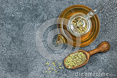 Herbal infusion fennel tea in glass tea pot with dried fennel seeds in wooden shovel on grey rustic table Stock Photo