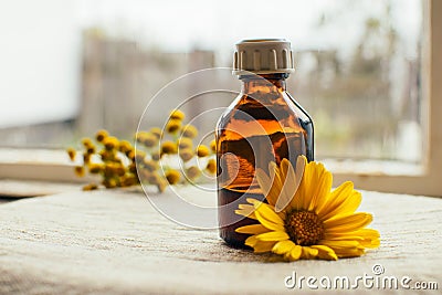 Herbal tincture in pharmacy bottle and yellow flower of calendula with tansy at background at linen textile, alternative medicine Stock Photo