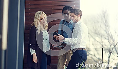 Here, take a look at this. three young businesspeople using a tablet while standing outside on the office balcony. Stock Photo