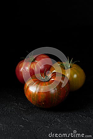 Hereditary tomatoes. Three tomatoes of different colors on a black textured background close-up Stock Photo