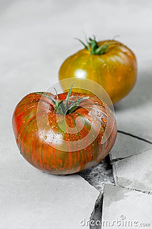 Hereditary tomatoes. Two tomatoes of different colors on a gray concrete table with a crack Stock Photo