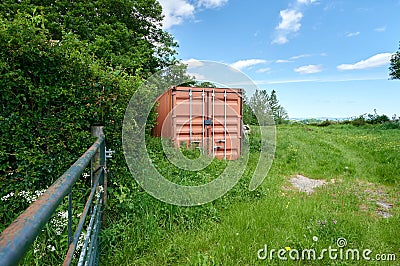 Herefordshire / UK - 6 June 2021: Mud coloured brown shipping container in Herefordshire field next to metal gate Editorial Stock Photo