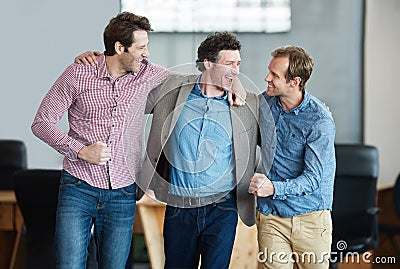 Heres to acing another project. a group of laughing coworkers standing arm in arm together in an office. Stock Photo