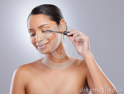 Heres to longer lashes. an attractive young woman standing alone in the studio and applying mascara. Stock Photo