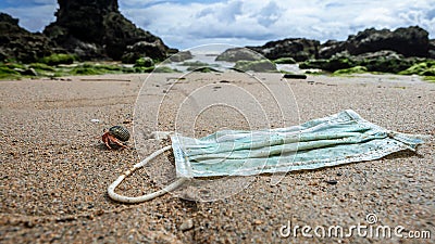 A hermit crab near medical waste, masks garbage trash on sea water. Covid-19 Stock Photo
